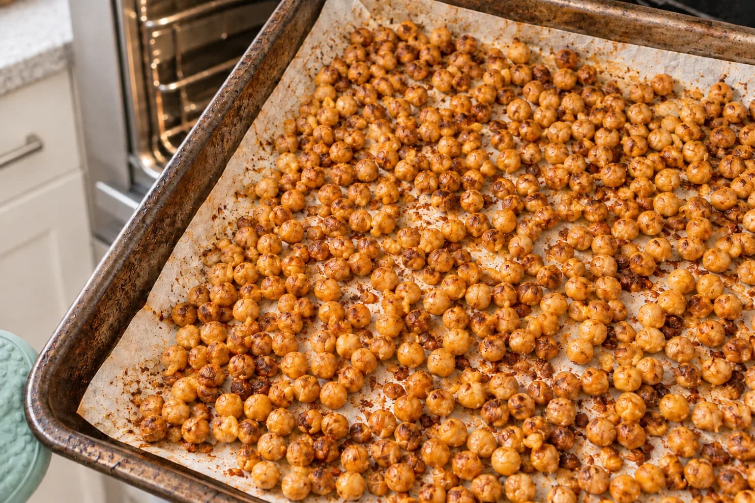 Hundreds of realistically sized BBQ chickpeas cooling on a used parchment-lined sheet pan