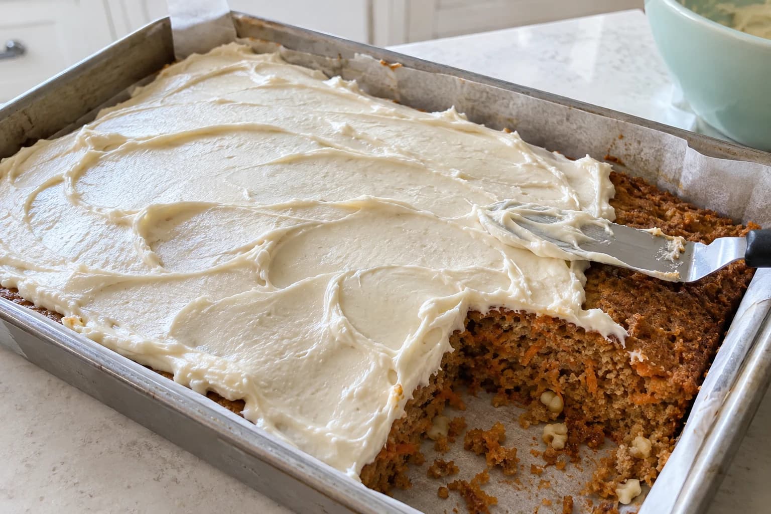 Cashew icing being spread unevenly over a carrot sheet cake in its baking pan