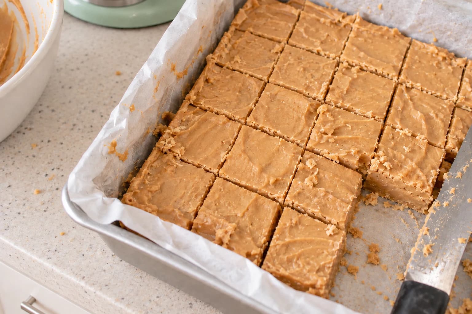Hand-cut peanut butter fudge in a parchment-lined metal pan with crumbs and one piece removed