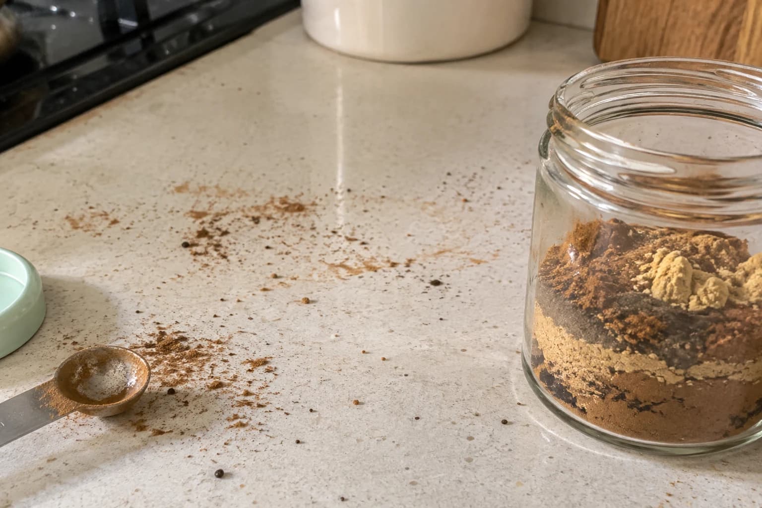 Gingerbread spices layered loosely in a small jar beside a used measuring spoon