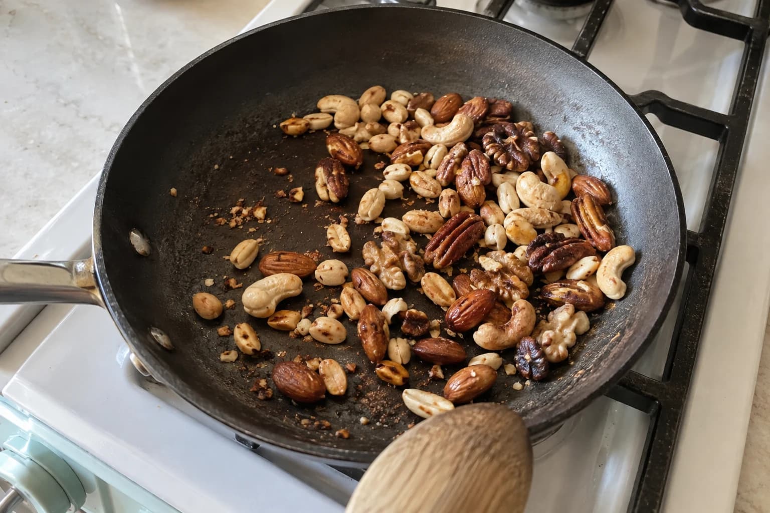 Five familiar nut varieties toasting loosely in a used frying pan