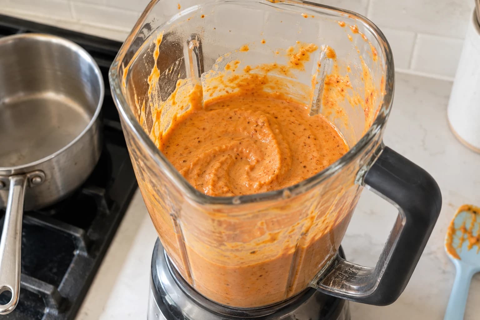 Thick orange vegan queso partway through blending in a household blender