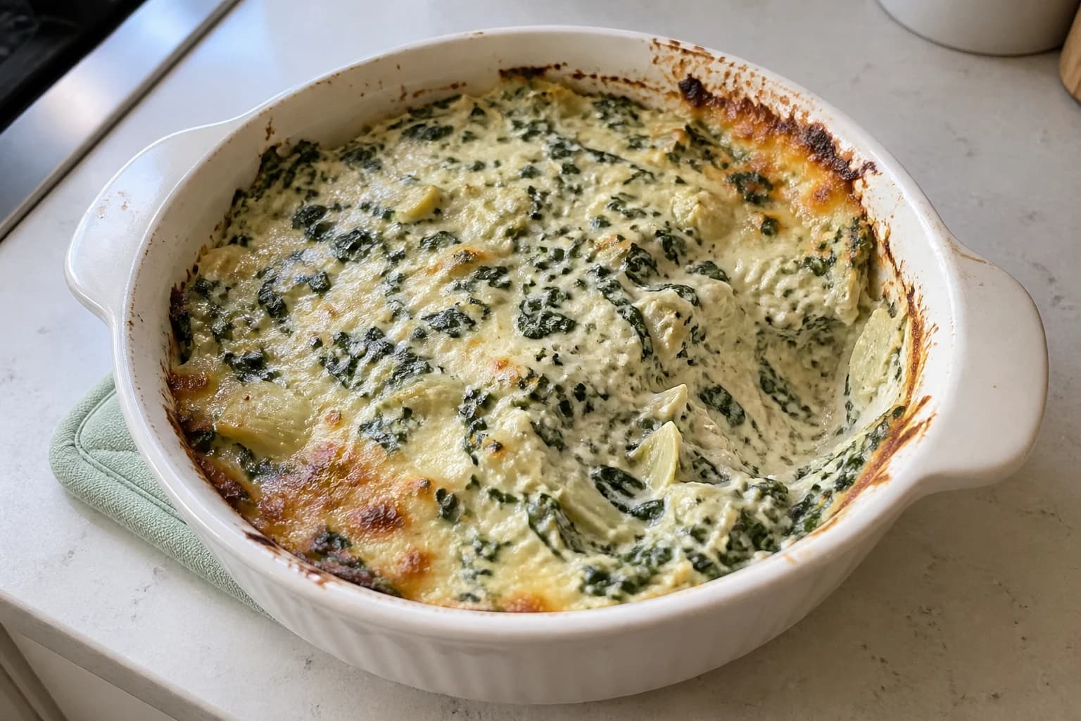 Hot spinach artichoke dip with a spoonful removed from one side of the baking dish