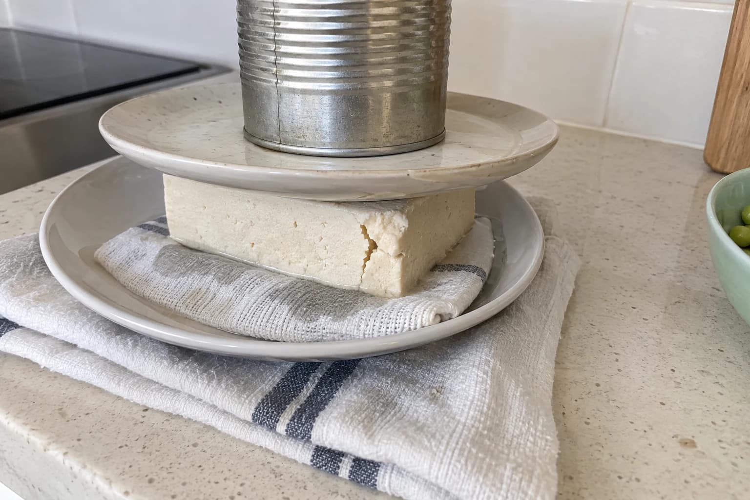 A block of tofu being pressed between two mismatched plates on a kitchen towel
