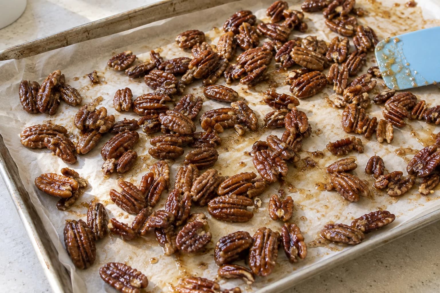 Maple-coated pecans cooling in a loose layer on a parchment-lined sheet pan