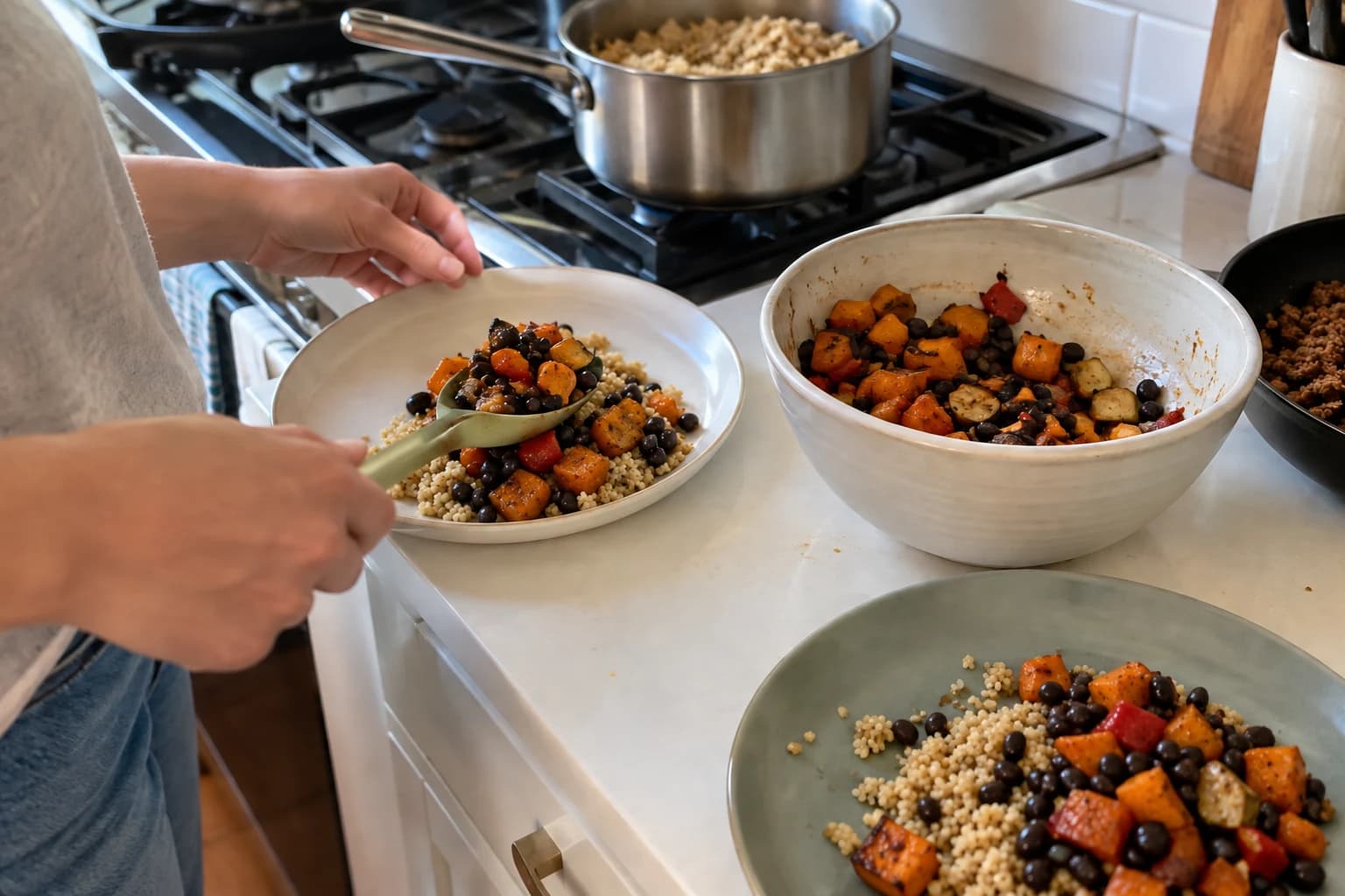 Two flexible grain bowls being assembled from beans and roasted vegetables beside a separate skillet